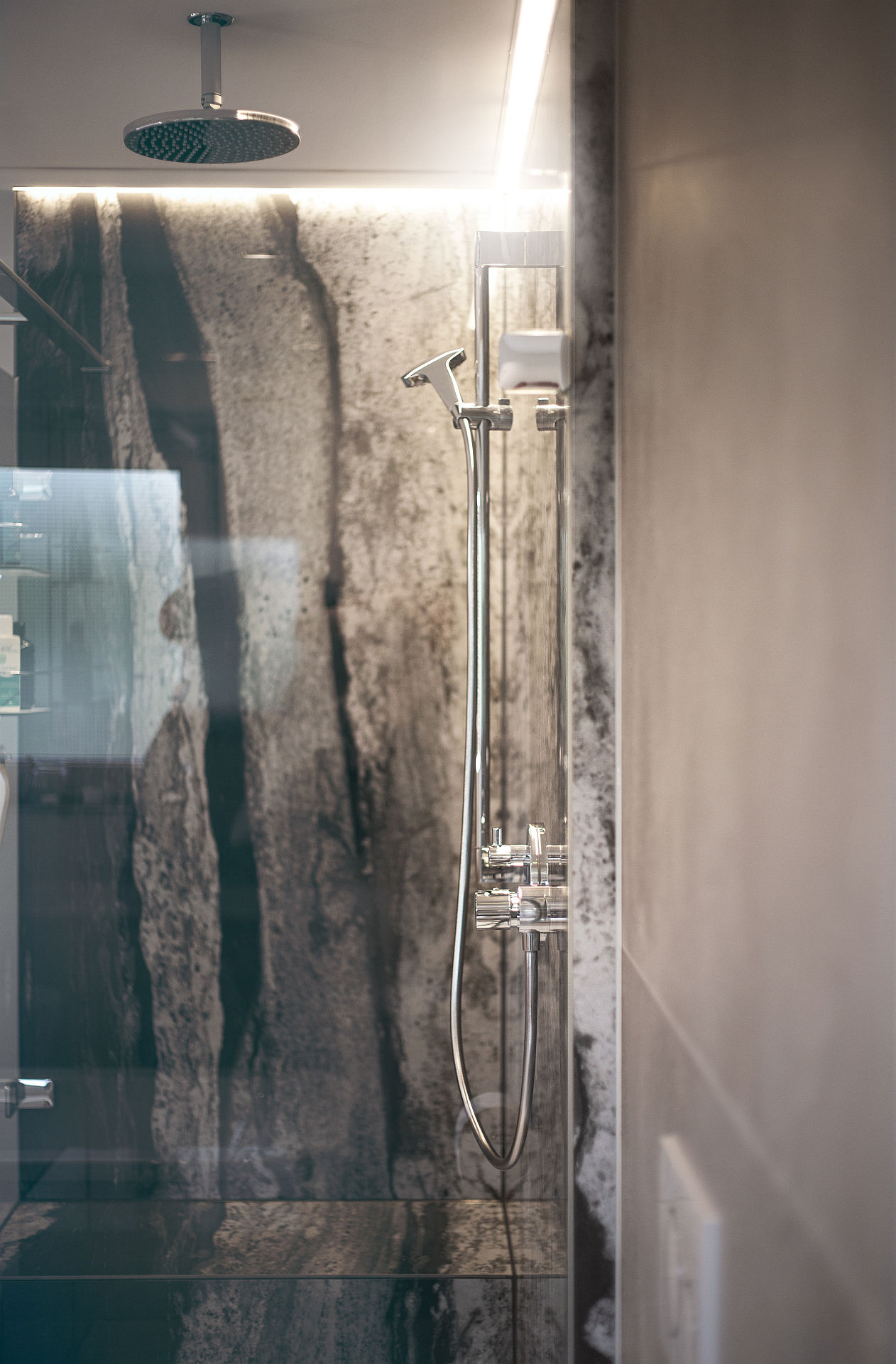 Detailaufnahme einer Dusche mit Natursteinwand und Regenduschkopfbrause.