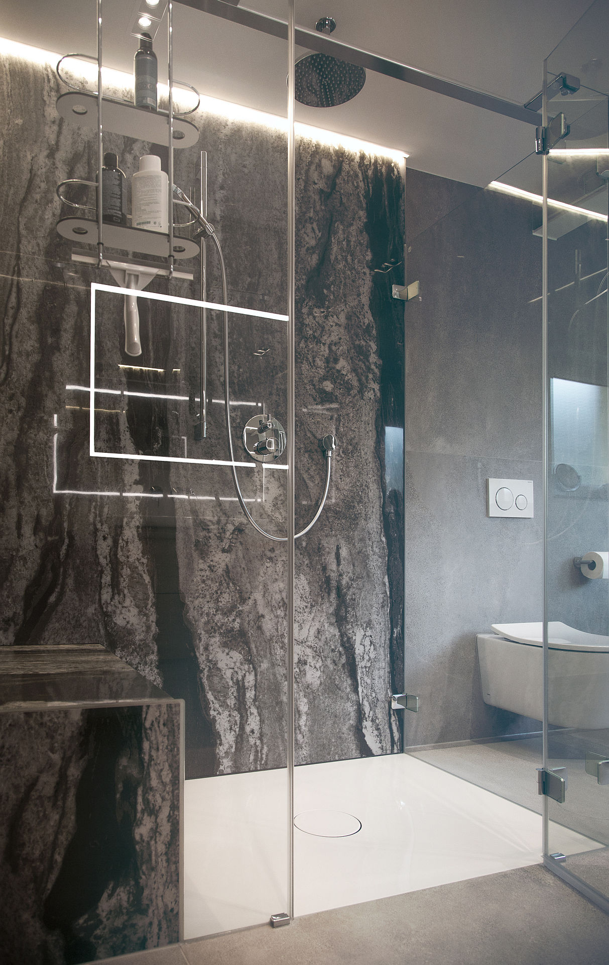 Luxuriöse begehbare Dusche mit Glaswand, Regenduschkopf und markanter Natursteinwand. Indirekte LED-Beleuchtung sorgt für eine edle Atmosphäre.