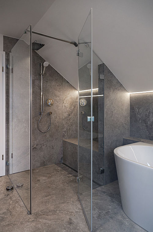 Bodenebene Walk-in-Dusche unter Dachschräge mit Sitzbank und grauen Natursteinfliesen.