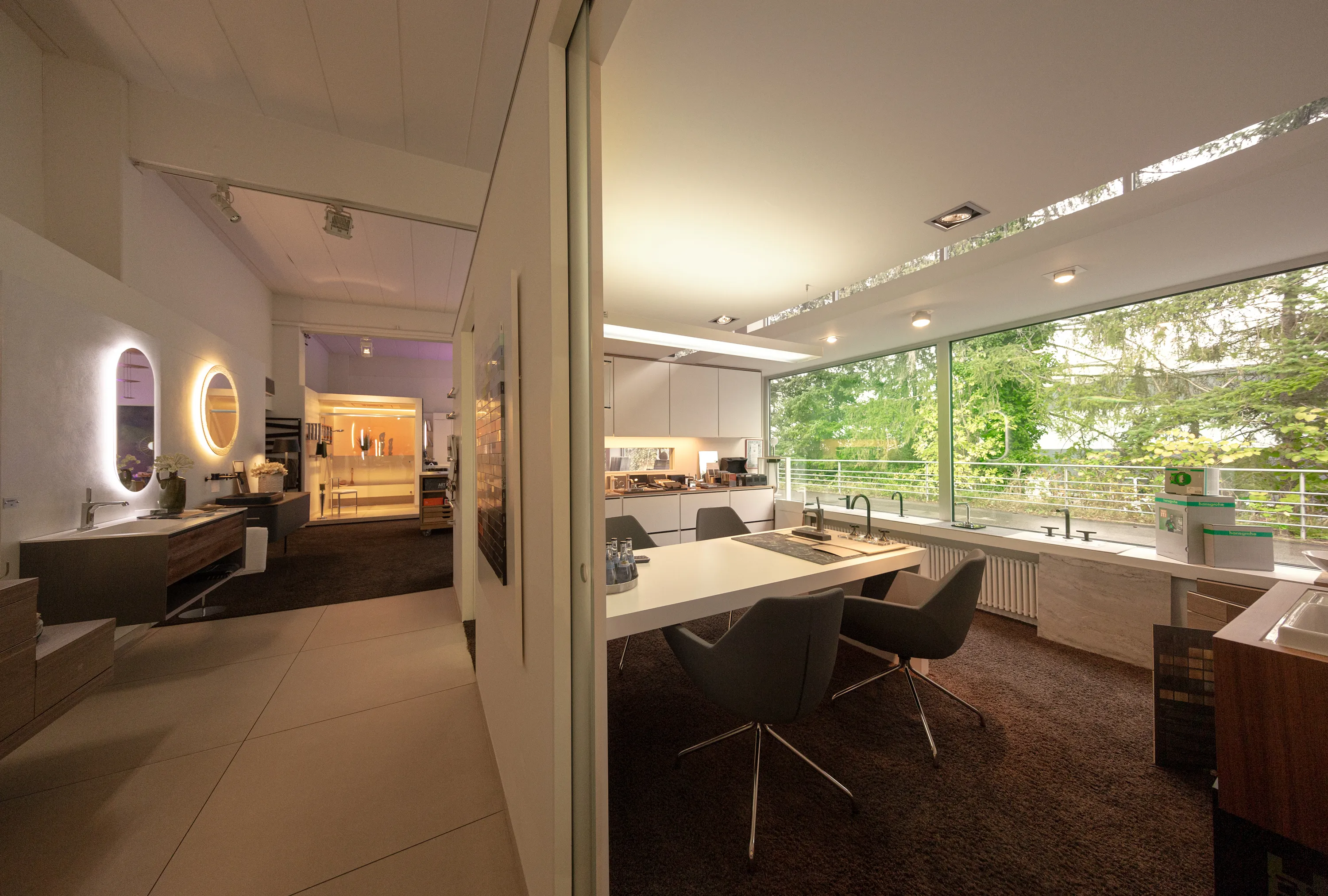 Ein modernes Badstudio mit großen Fensterfronten, die viel natürliches Licht in den Raum lassen und den Blick auf grüne Bäume freigeben. 