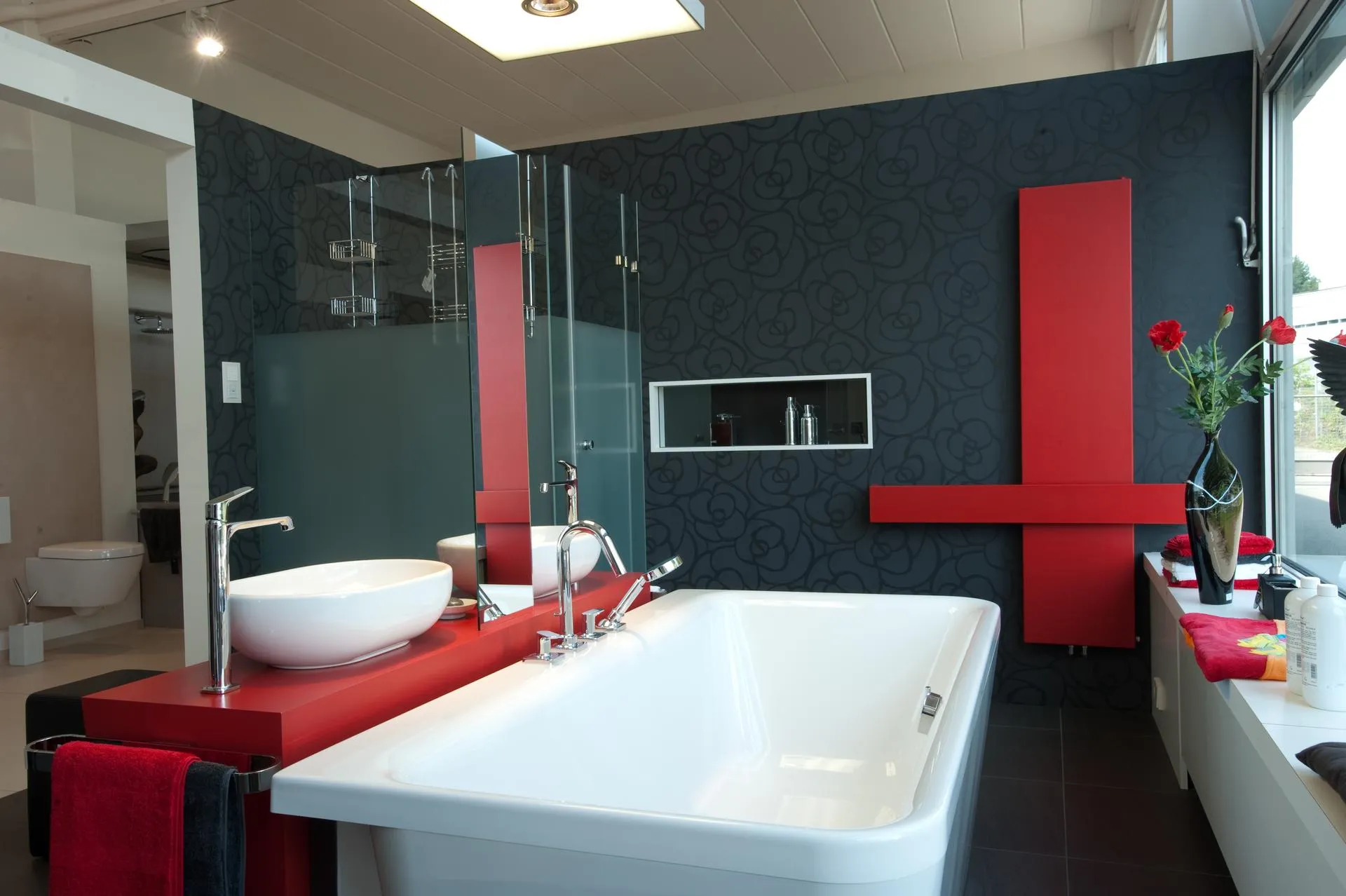 Ein modernes Badezimmer mit einer freistehenden weißen Badewanne und einer auffälligen, roten Konsole, auf der ein elegantes Waschbecken und Armaturen platziert sind.