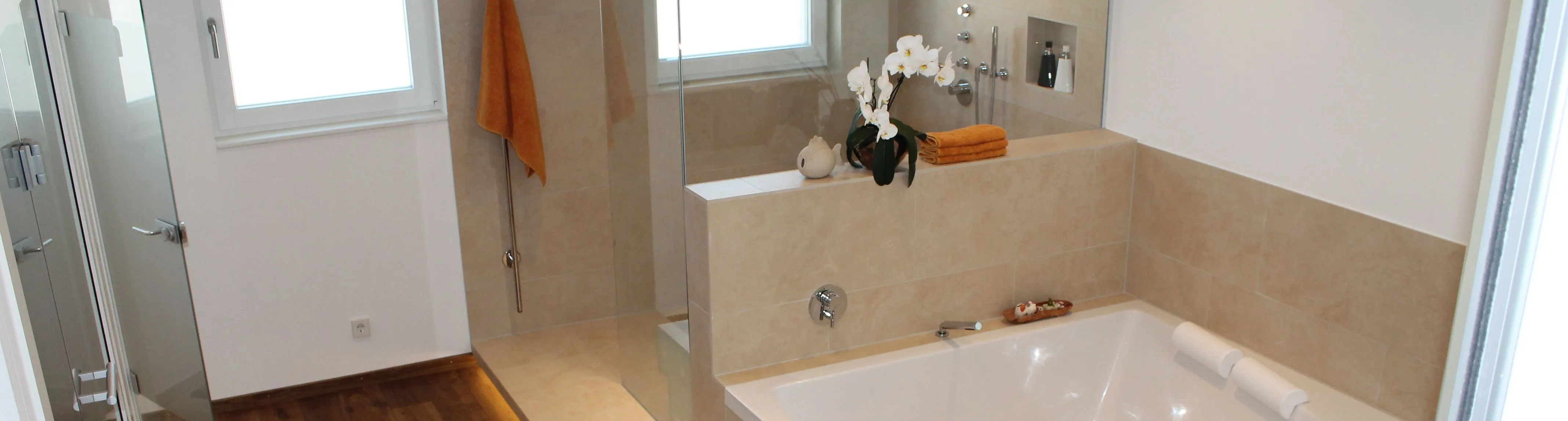 Badezimmer mit einer Badewanne, beigen Natursteinfliesen und einer modernen Dusche mit Glaswand.