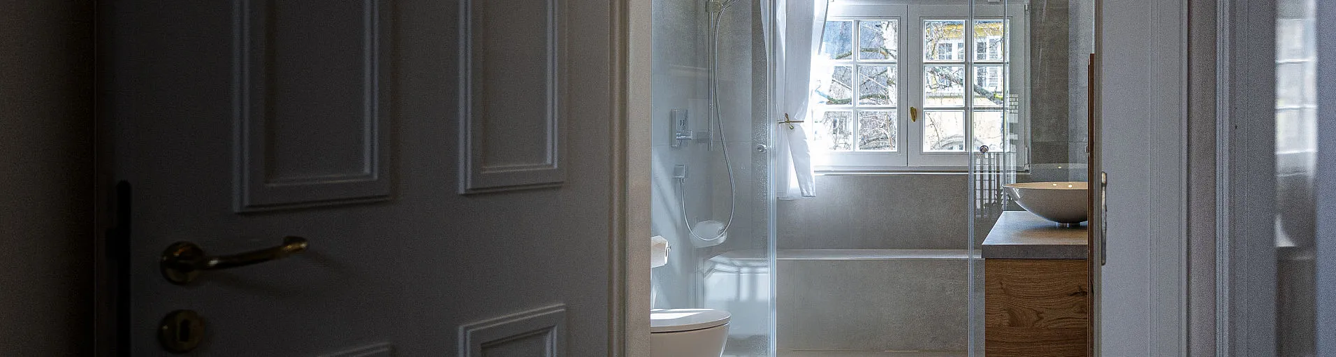 Ein stilvoller Durchgang mit einer klassischen Jugendstil-Tür führt in ein modernes Badezimmer mit natürlichen Materialien.