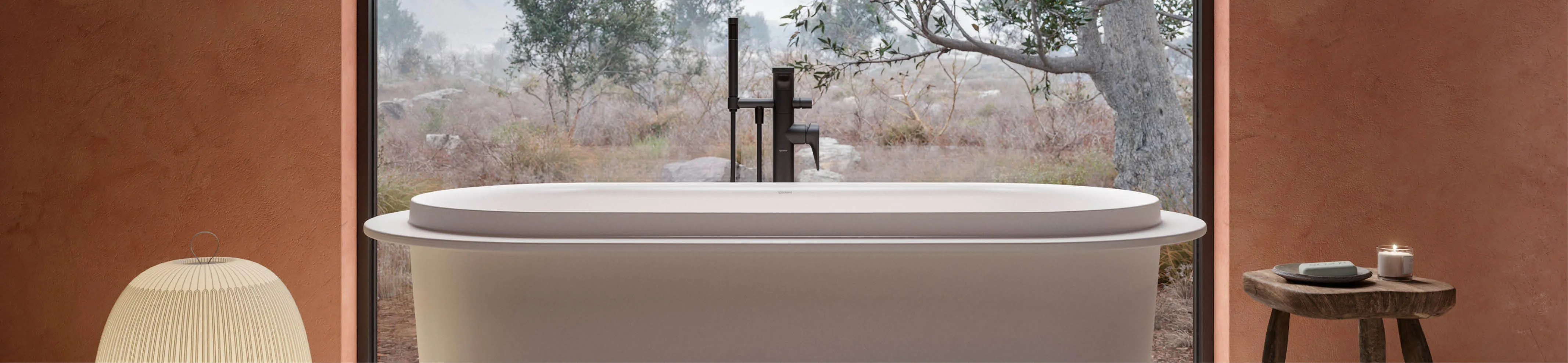 Auf Headergröße zugeschnittene freistehende Badewanne Vitrium der Marke Duravit vor Panoramafenster mit Blick in die Natur in ruhigem Badezimmerdesign.