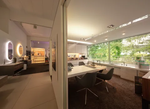 Ein modernes Badstudio mit großen Fensterfronten, die viel natürliches Licht in den Raum lassen und den Blick auf grüne Bäume freigeben. 