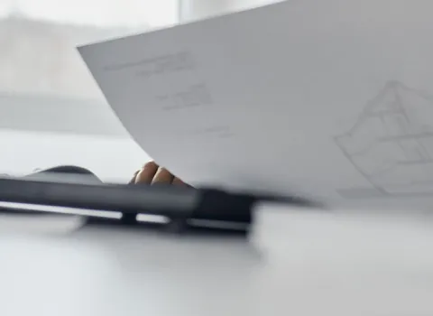 Eine Nahaufnahme eines Arbeitsplatzes zeigt eine Person, die technische Pläne in der Hand hält.