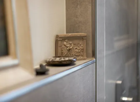 Eine schmale Ablage im Badezimmer mit antikem Relief und kleinen Dekosteinen.