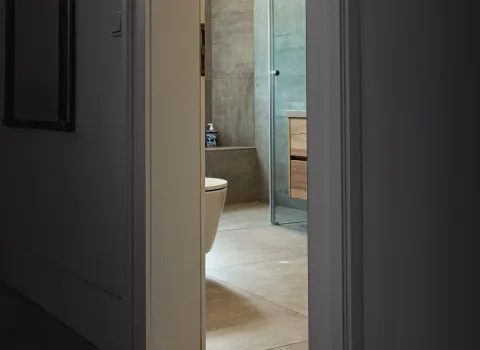 Ein dunkler Flur mit historischer Jugendstil-Tür öffnet sich zu einem hellen, modernen Badezimmer.