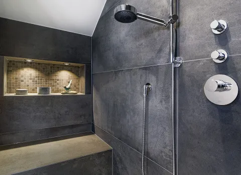 Eine luxuriöse, begehbare Dusche mit dunklen Steinfliesen, einer integrierten Sitzbank und verchromter Duscharmatur.