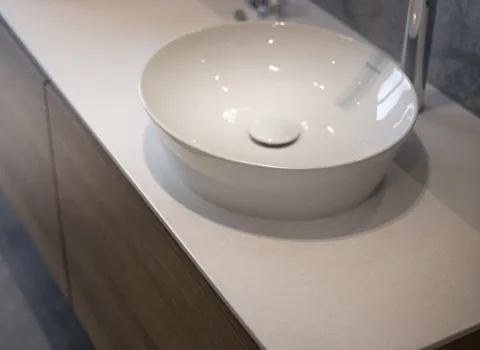 Ein rundes, weißes Aufsatzwaschbecken sitzt elegant auf einer hellen Waschtischplatte mit Holzfronten.