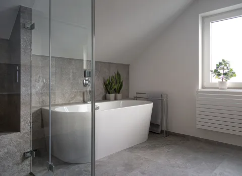 Dachbadezimmer mit wandmontierter Badewanne und grauen Natursteinfliesen in neutralen Grautönen.