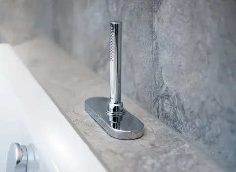 Ein verchromtes Wannen-Einlaufventil ist flach auf einer natursteinverkleideten Ablage über der Badewanne installiert.