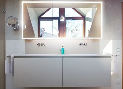 Doppelwaschtisch mit großem Spiegelschrank in dem sich das Badfenster spiegelt