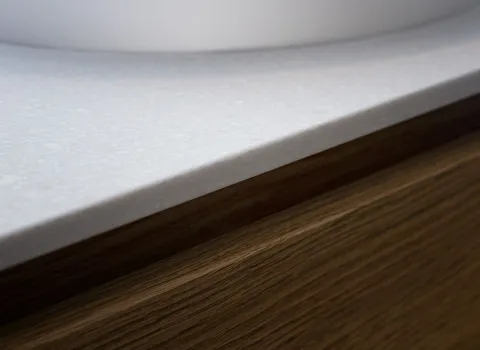 Eine helle Waschtischplatte mit glatter, leicht strukturierter Oberfläche trifft auf einen Unterschrank aus echtem Holz mit sichtbarer Maserung..