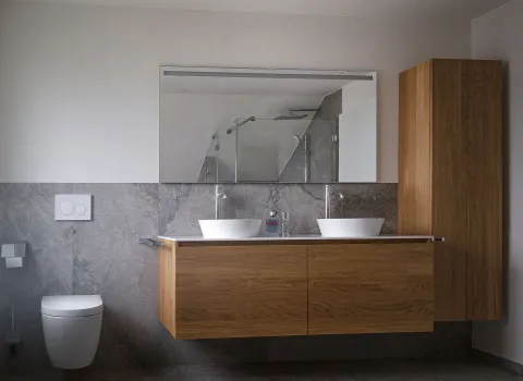 Ein moderner Waschtisch aus Holz mit zwei Aufsatzwaschbecken steht vor einer Wand aus grauem Naturstein.