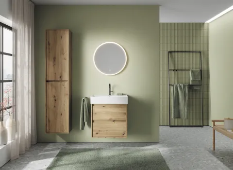 Badezimmer mit grünen Wänden und Waschtisch, Badschrank und rundem Leuchtspiegel aus der Badmöbel-Kollektion Devio des Herstellers Burgbad.