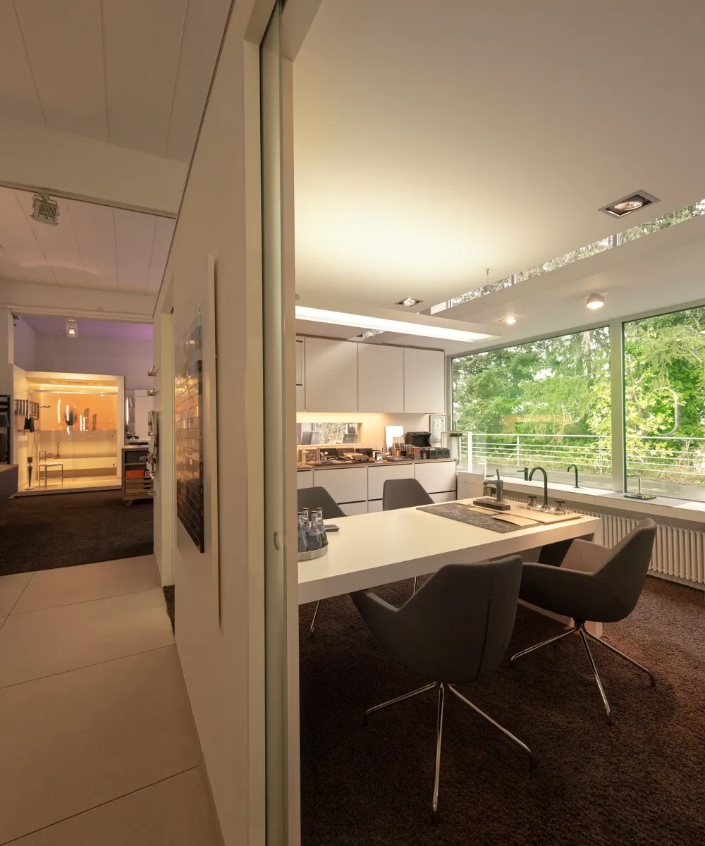 Ein modernes Badstudio mit großen Fensterfronten, die viel natürliches Licht in den Raum lassen und den Blick auf grüne Bäume freigeben. 