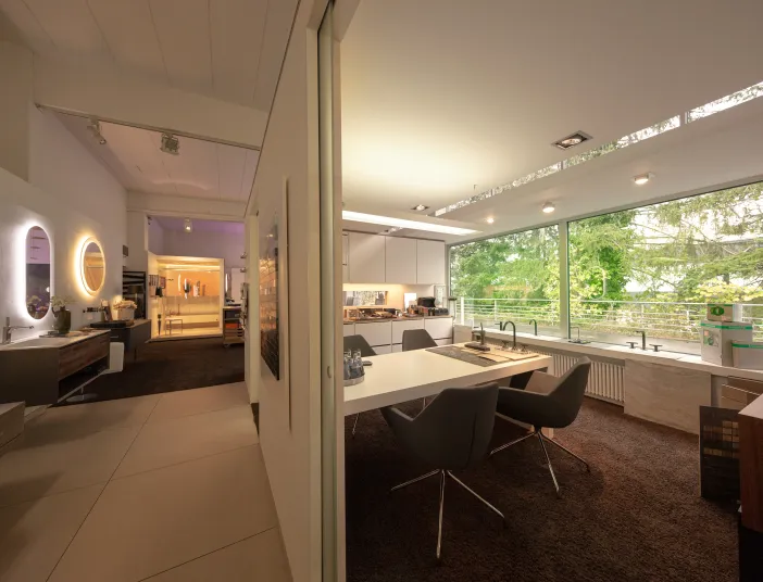 Ein modernes Badstudio mit großen Fensterfronten, die viel natürliches Licht in den Raum lassen und den Blick auf grüne Bäume freigeben. 
