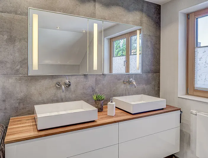 Stilvolles Badezimmer mit zwei rechteckigen Aufsatzwaschbecken auf einer Holzkonsole und einer grau gefliesten Wand. 
