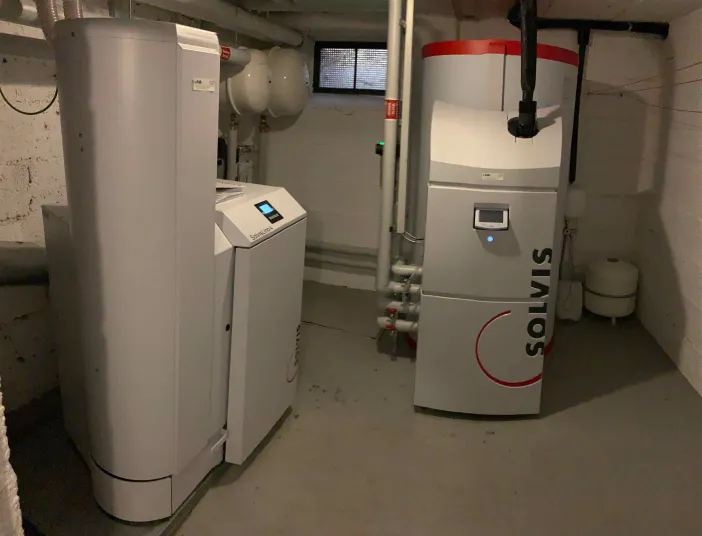 Das Bild zeigt eine moderne Heizungsanlage der Marke Solvis mit zwei weißen Hauptgeräten und einem großen Pufferspeicher mit rotem Deckel. 